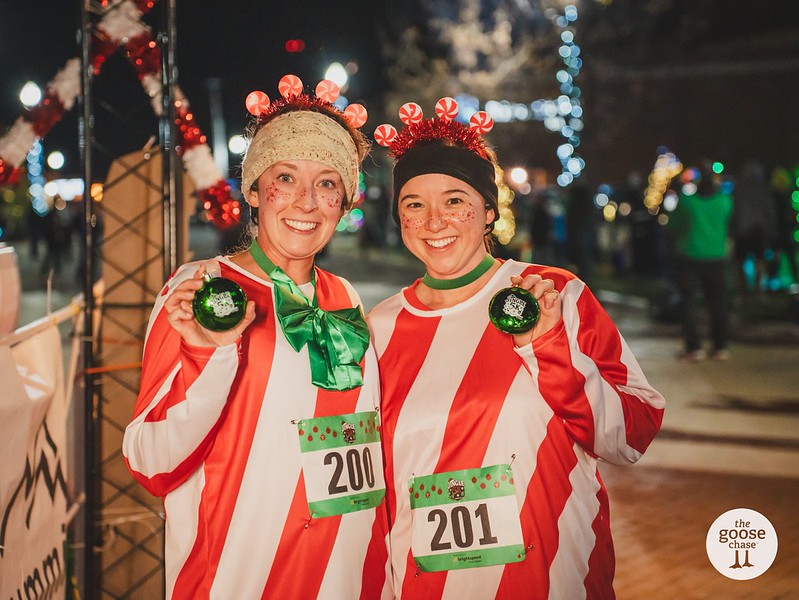 Two participants in red and white costumes hold their past-event medals at a past Jingle event