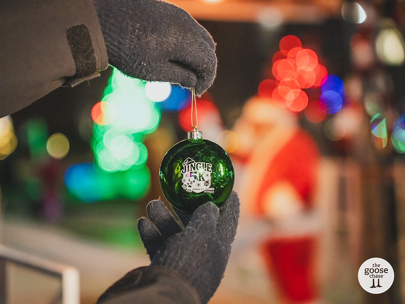 Gloved hands hold a green ornament-style Jingle 5K medal from a past event