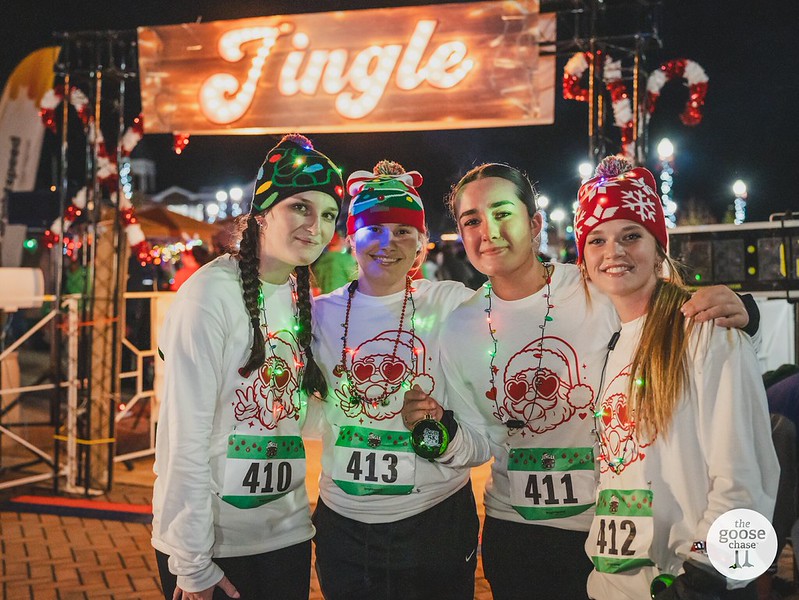 Four participants in matching Santa shirts and festive hats pose beneath a Jingle sign at a past event