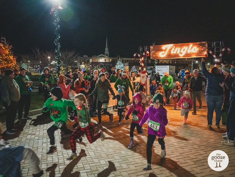 Children and adults set off beneath the illuminated Jingle sign at a past nighttime event
