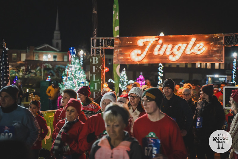 Runners and walkers stream beneath the illuminated Jingle sign and a Believe banner at a past nighttime Jingle event