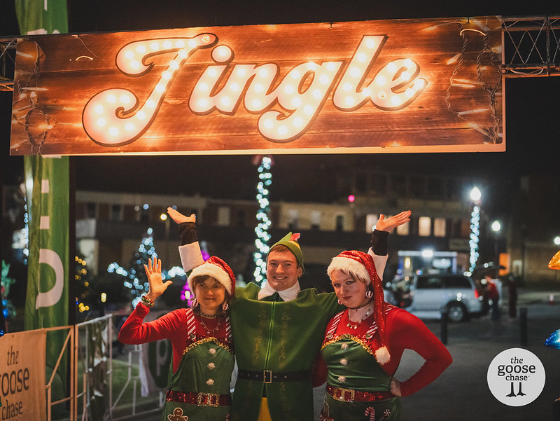 Jingle volunteers in festive outfits beneath the illuminated Jingle sign