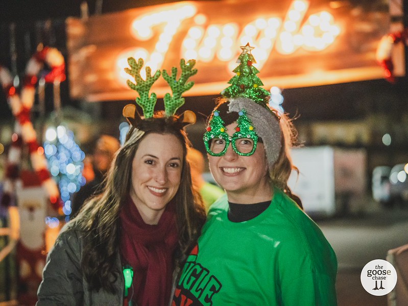 Two smiling participants wear reindeer antlers and Christmas tree accessories at a past Jingle event
