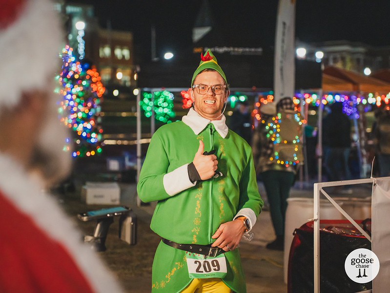 A participant in a green elf outfit smiles at a past Jingle event