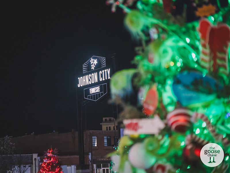 The illuminated Johnson City Tennessee sign glows at night beside a bright green holiday tree and a smaller red tree at a past Jingle event